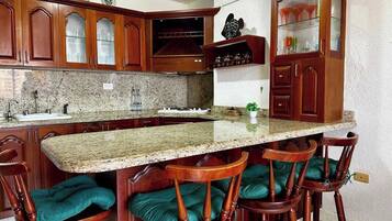 A kitchen with granite countertops, wooden cabinets, and bar stools with cushioned seats.