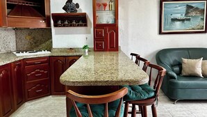 Une cuisine dotée d’un plan de travail en granit, de meubles en bois, d’un coin repas avec des chaises et d’un canapé vert.