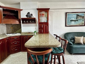 Una cocina con encimera de granito, armarios de madera, un comedor con sillas y un sofá verde.