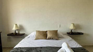 Ein Hotelzimmer mit einem Bett, zwei Nachttischlampen, einem zusammengerollten Handtuch und einer gemusterten Decke.