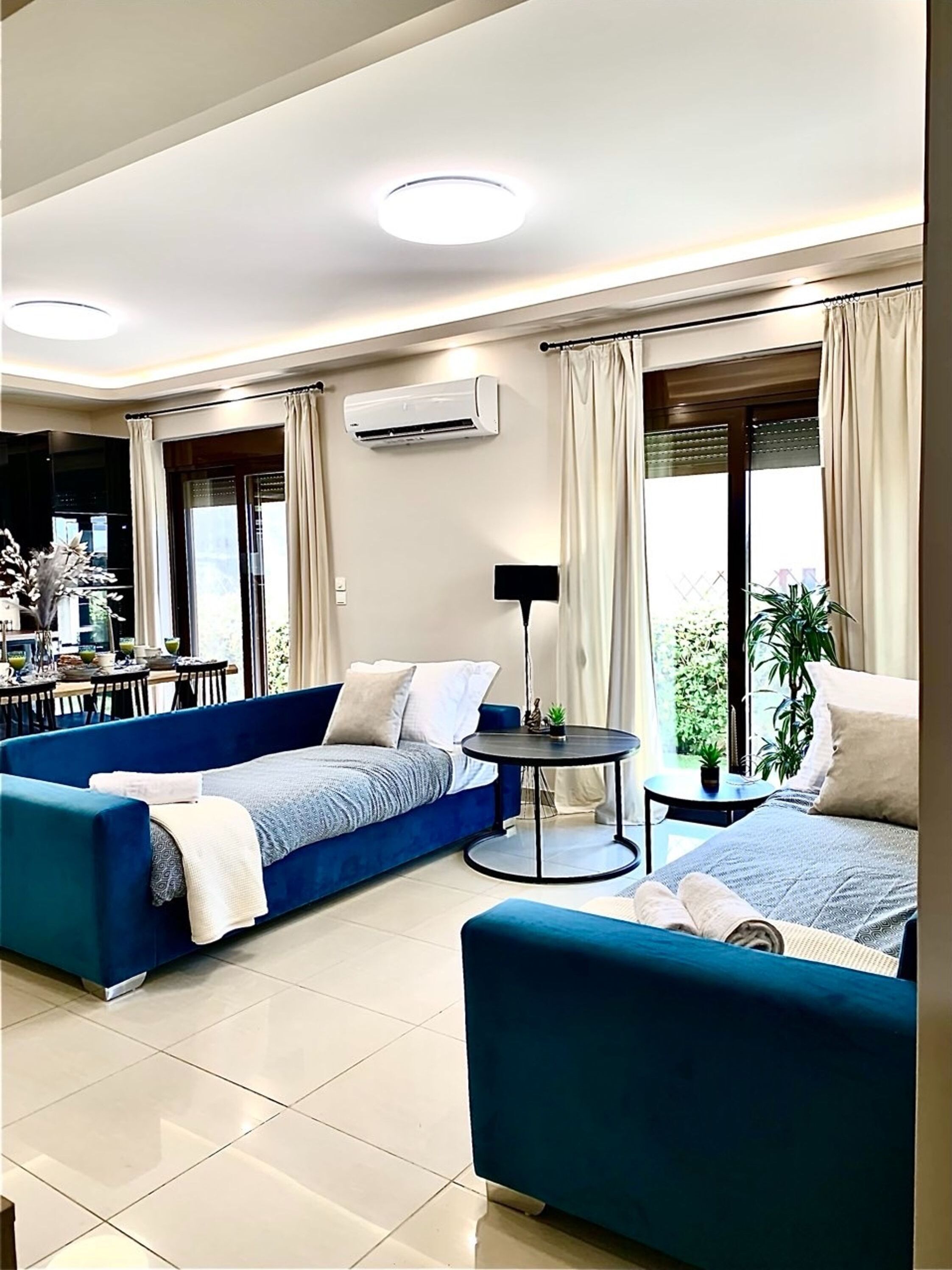 A modern living room with a blue sofa, a small round table, and a large window with curtains.