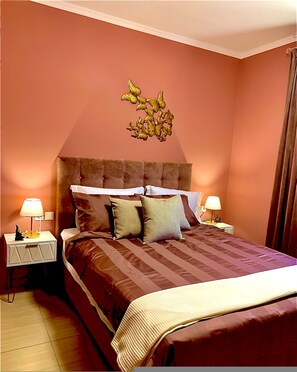 Camera da letto con testiera trapuntata, un letto grande con biancheria a righe, due comodini con lampade e un elemento decorativo a parete.