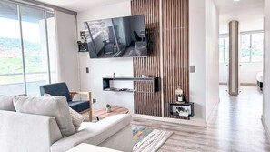 Een moderne woonkamer met een flatscreen televisie aan de wand, een bank, een fauteuil en een bijzettafeltje met een plant.