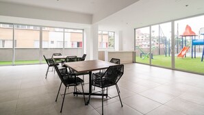 A spacious indoor area with a large table and chairs, large windows, and a view of a playground outside.