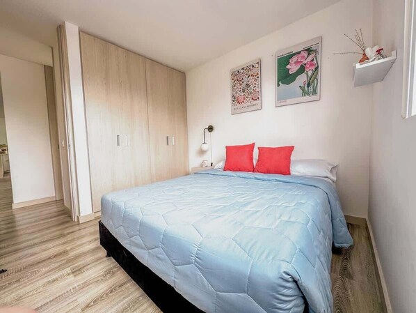 A bedroom with a bed, a wardrobe, and two wall-mounted pictures.