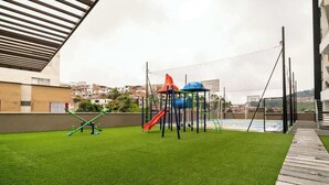An outdoor play area with artificial grass, a slide, and a climbing structure.