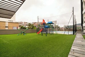 An outdoor play area with artificial grass, a slide, and a climbing structure.