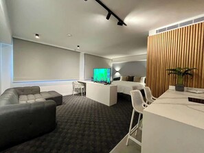 A modern hotel room with a large bed, a desk, a television, and a seating area with a sofa and chairs. - Altamira Apartment: Newly Remodeled, Balcony, (Caracas)