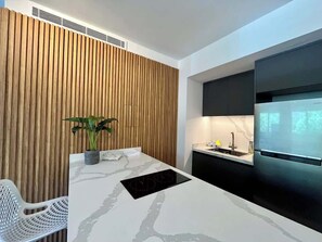 A modern kitchen with a wooden slat wall, a white countertop, a built-in stove, and a black refrigerator. - Altamira Apartment: Newly Remodeled, Balcony, (Caracas)