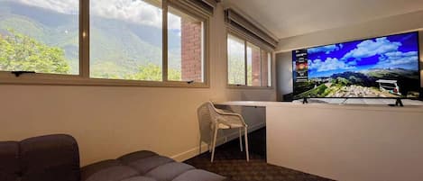 A room with a large window, a flat-screen TV, a sofa, and a desk with a chair.