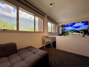 A room with a large window, a flat-screen TV, a sofa, and a desk with a chair. - Altamira Apartment: Newly Remodeled, Balcony, (Caracas)