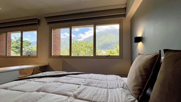 Una camera da letto con un letto grande, due finestre, una lampada a parete e vista su del verde.