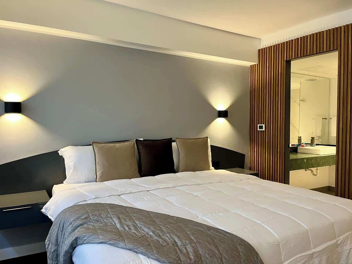 Une chambre d’hôtel avec un grand lit, des tables de chevet, un miroir et des lampes fixées au mur.