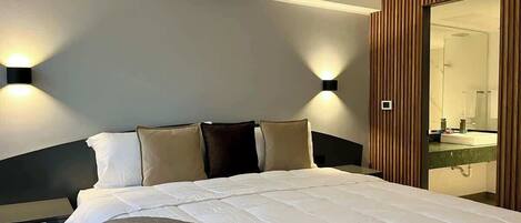 Habitación de hotel con una cama grande, mesitas de noche, un espejo y lámparas de pared.