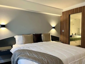 Een hotelkamer met een groot bed, nachtkastjes, een spiegel en wandlampen.