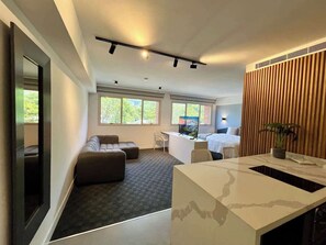 A modern hotel room with a sofa, a desk, a bed, and a large window. - Altamira Apartment: Newly Remodeled, Balcony, (Caracas)