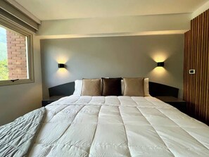 Una cama bien tendida con una colcha acolchada, dos lámparas de noche y una ventana a la izquierda.