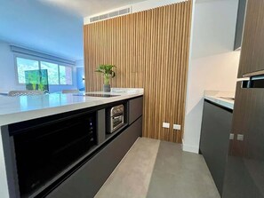 A modern kitchen with a built-in oven, a sink, and a wooden accent wall. - Altamira Apartment: Newly Remodeled, Balcony, (Caracas)