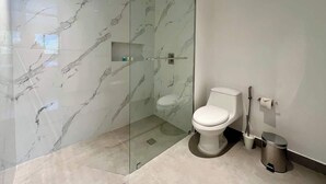 Un bagno moderno con doccia vetro, un WC e un cestino.