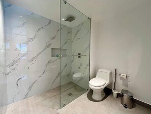 A modern bathroom with a glass-enclosed shower, a toilet, and a trash bin. - Altamira Apartment: Newly Remodeled, Balcony, (Caracas)