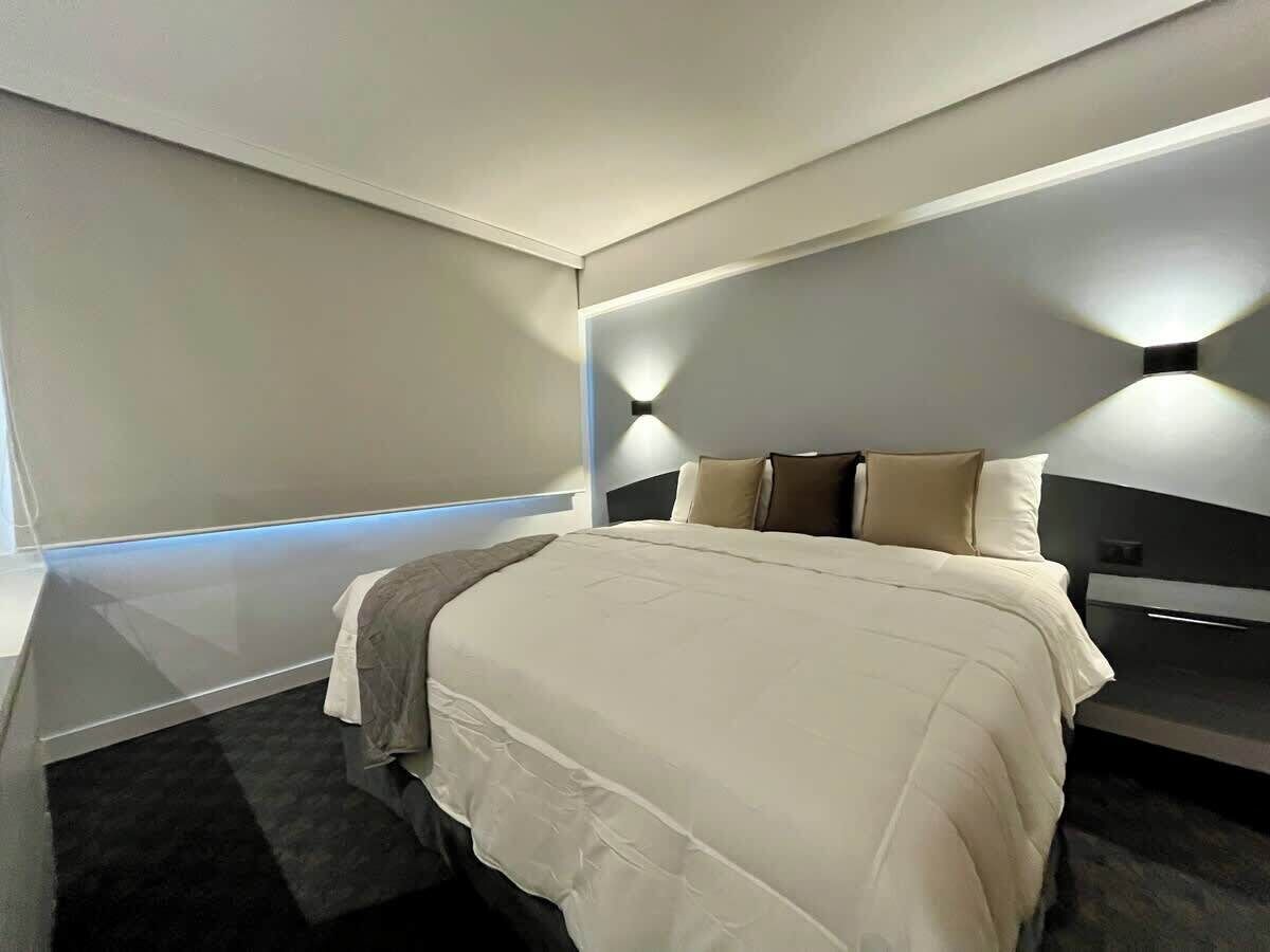 Ein modernes Hotelzimmer mit einem großen Bett, Nachttischen und integrierter Beleuchtung.