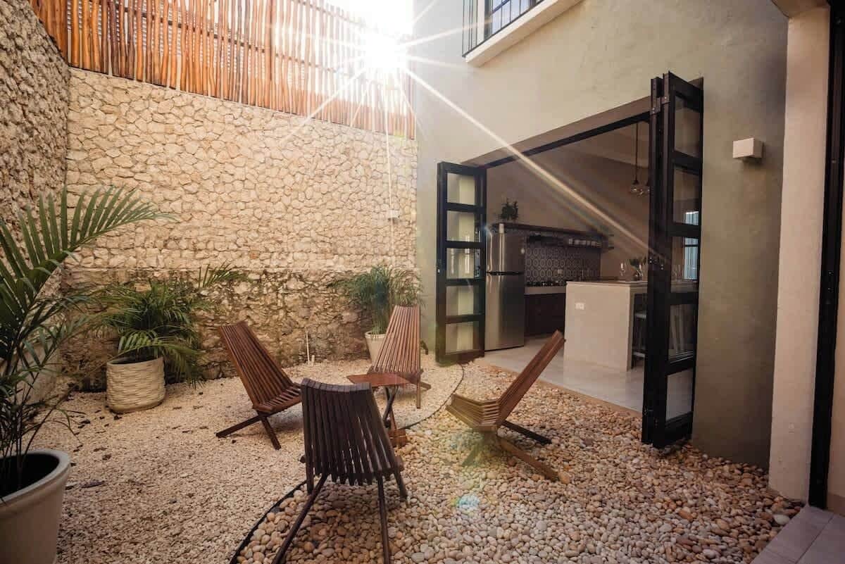 An outdoor patio with a stone wall, a wooden table, and two chairs.