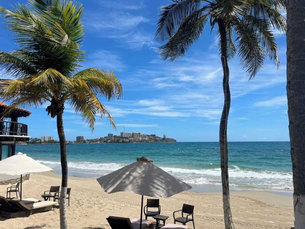 Une plage avec des palmiers, un parasol et des chaises longues.