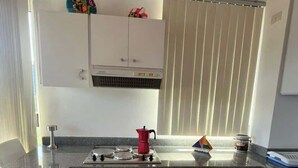 A kitchen with white cabinets, a stove, a red coffee pot, and a striped rug on the floor. - Tu Refugio Porlamar | A pasos de Playa Veleros (Porlamar)