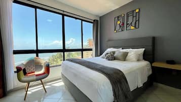 Un dormitorio con un ventanal grande, una cama, una silla y obras de arte en la pared.