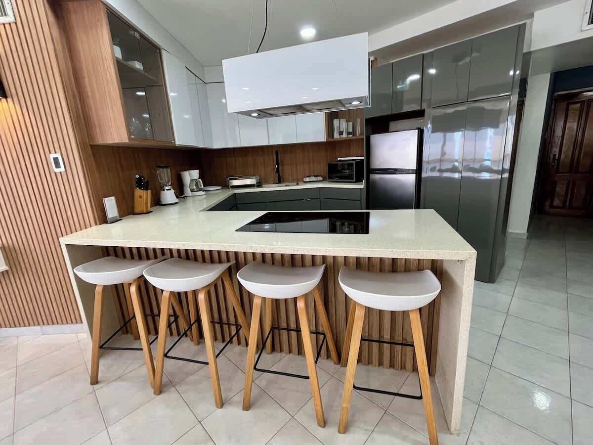 Una cocina moderna con una isla central, taburetes de bar y electrodomésticos de acero inoxidable.