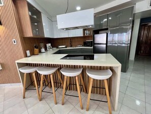 Une cuisine moderne dotée d’un îlot central, de tabourets de bar et d’appareils électroménagers en acier inoxydable.