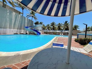 Une piscine avec un toboggan, des chaises longues et des palmiers en arrière-plan.