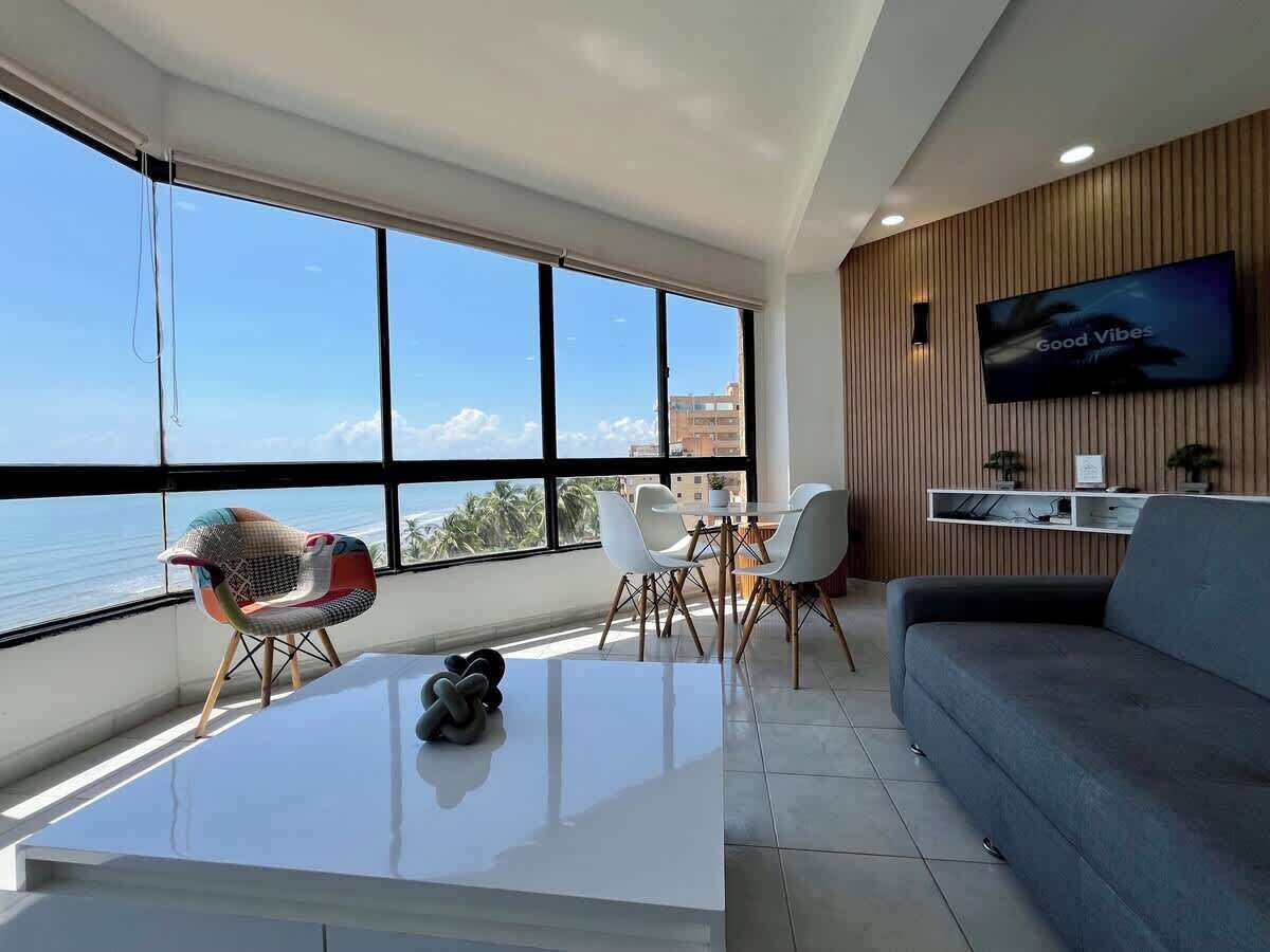 A modern living room with a large window, a flat-screen TV, and a dining area.