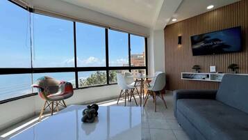 A modern living room with a large window, a flat-screen TV, and a dining area.