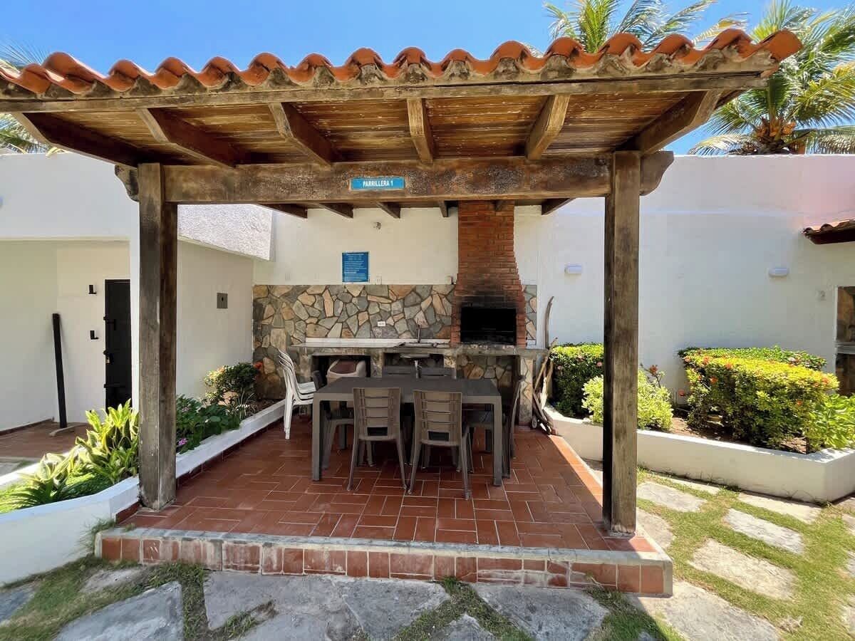 Un patio al aire libre con chimenea de piedra, una pérgola de madera y una mesa de comedor con sillas.