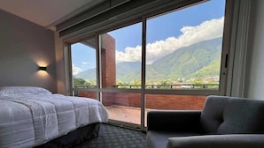Una camera d'albergo con un letto, una sedia e un'ampia finestra che offre vista sulle montagne.