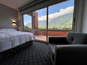 A hotel room with a bed, a chair, and a large window offering a mountain view. - PH Altamira: Vistas Ávila & Terraza Panorámica (Caracas)