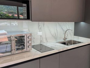A modern kitchen with a built-in toaster oven, a sink, and a window with a view of buildings. - PH Altamira: Vistas Ávila & Terraza Panorámica (Caracas)