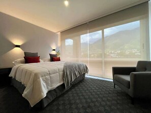 A hotel room with a large bed, a chair, a desk with a lamp, and a view of the outdoors. - PH Altamira: Vistas Ávila & Terraza Panorámica (Caracas)