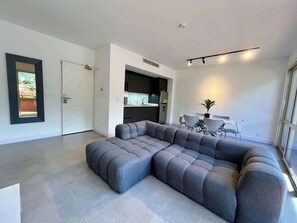 A modern living room with a sectional sofa, a dining area with a table and chairs, and a kitchen in the background. - PH Altamira: Vistas Ávila & Terraza Panorámica (Caracas)