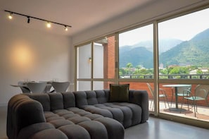 A modern living room with a sectional sofa, a dining table with chairs, and a balcony with a view of mountains. - PH Altamira: Vistas Ávila & Terraza Panorámica (Caracas)