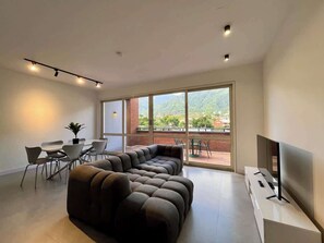 A modern living room with a sectional sofa, a flat-screen TV, and a dining area with chairs and a table. - PH Altamira: Vistas Ávila & Terraza Panorámica (Caracas)