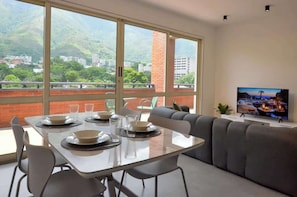 Ein modernes Wohnzimmer mit Essbereich, großen Fenstern und einem Fernseher.