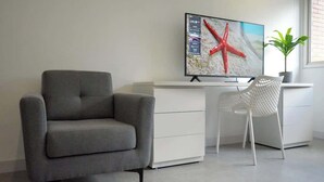 A modern living room with a grey sofa, a white desk, and a flat-screen TV mounted on the wall. - Romantic Altamira Apt: Fast WiFi & Privacy (Caracas)