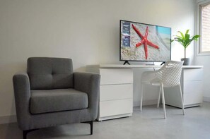 A modern living room with a grey sofa, a white desk, and a flat-screen TV mounted on the wall. - Romantic Altamira Apt: Fast WiFi & Privacy (Caracas)