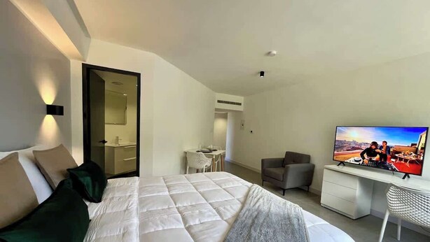 A hotel room with a bed, a desk, a television, and a bathroom visible through an open door. - Romantic Altamira Apt: Fast WiFi & Privacy (Caracas)