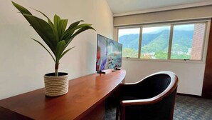 Ett rum med ett skrivbord, en stol, en tv och ett fönster med utsikt över ett berg.