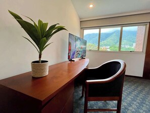 Ein Zimmer mit Schreibtisch, Stuhl, Fernseher und einem Fenster mit Bergblick.