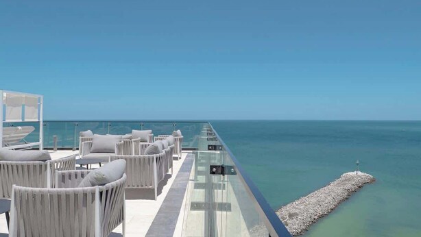 A seaside terrace with white wicker furniture and a glass balustrade overlooking the ocean. - Dpto. de 2 Hab. Frente a la Playa & Amenidades Top (Progreso)