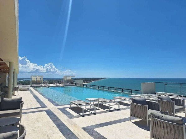 A rooftop pool area with lounge chairs and a view of the ocean.
